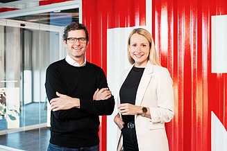 A man and a woman stand and smile at the camera.