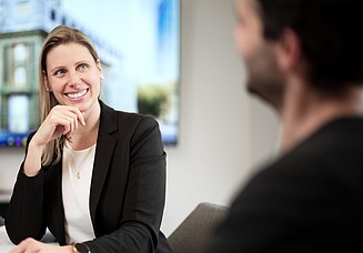 A woman in the office listening to a colleague with an interested smile