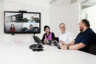The IT Purchasing team has a meeting, with four IT purchasers present digitally and three IT purchasers in person.