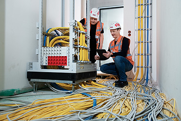 Zwei Kollegen prüfen in einem Rohbau eine Netzwerkverkabelung.