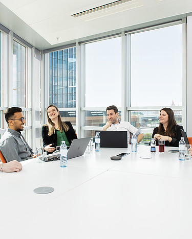 Ein Team sitzt in einem hellen Konferenzraum an einem Tisch vor einer Fensterfront.