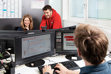 Ein Kollege und eine Kollegin betrachten etwas an einem Bildschirmarbeitsplatz.