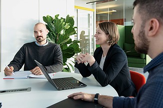 Three STRABAG employees sit together at a table with laptops