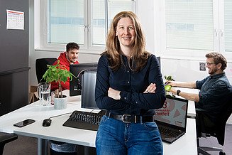 Die Gruppenleiterin IT-Projektmanagement ist im Fokus, während hinten zwei Kollegen an IT Project Manager Tasks arbeiten. 