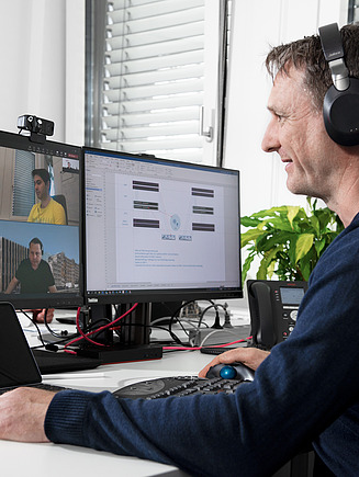 A man sits at a desk and takes part in a video conference.